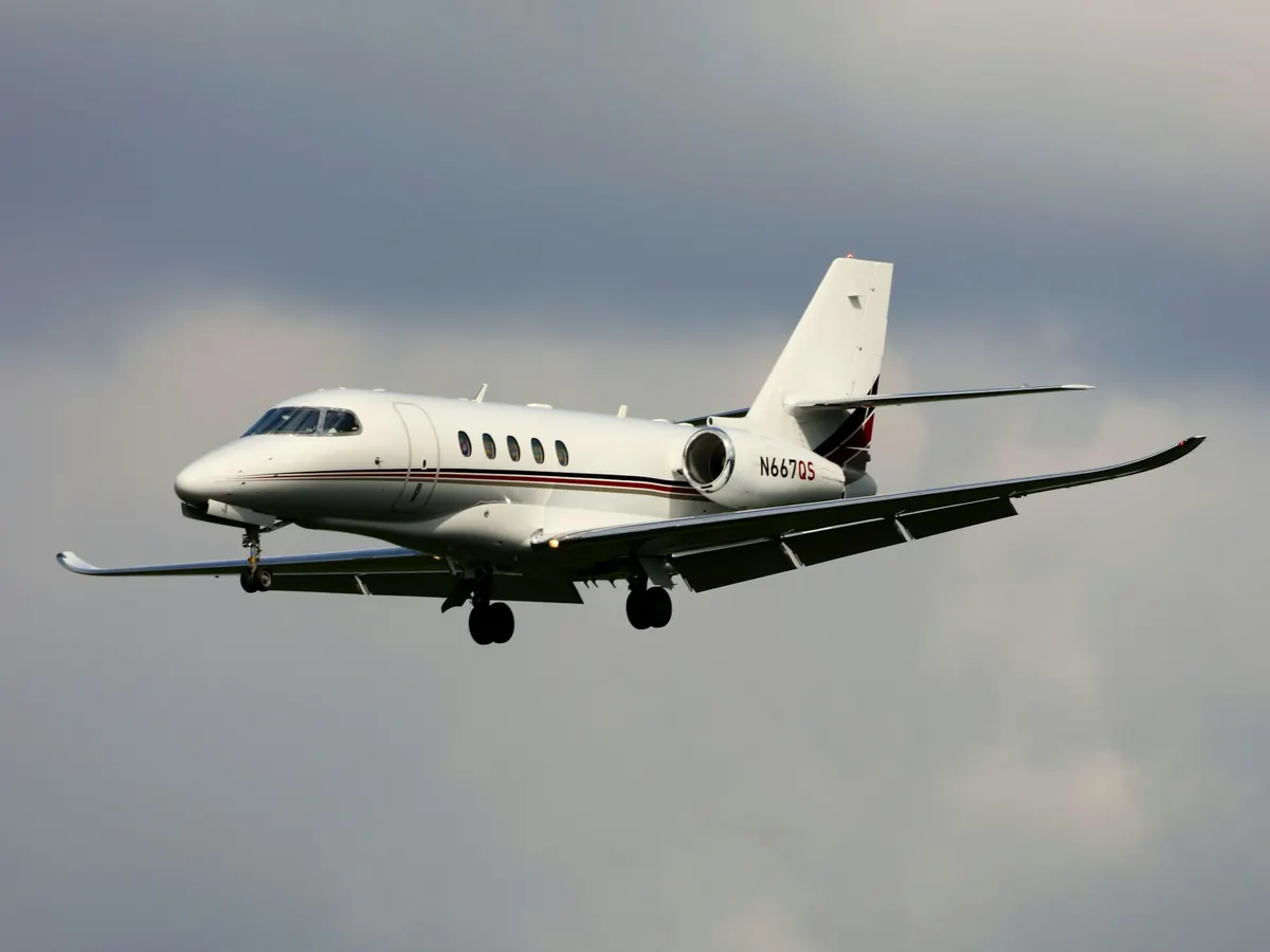 Business jet in flight with landing gear down against a cloudy sky